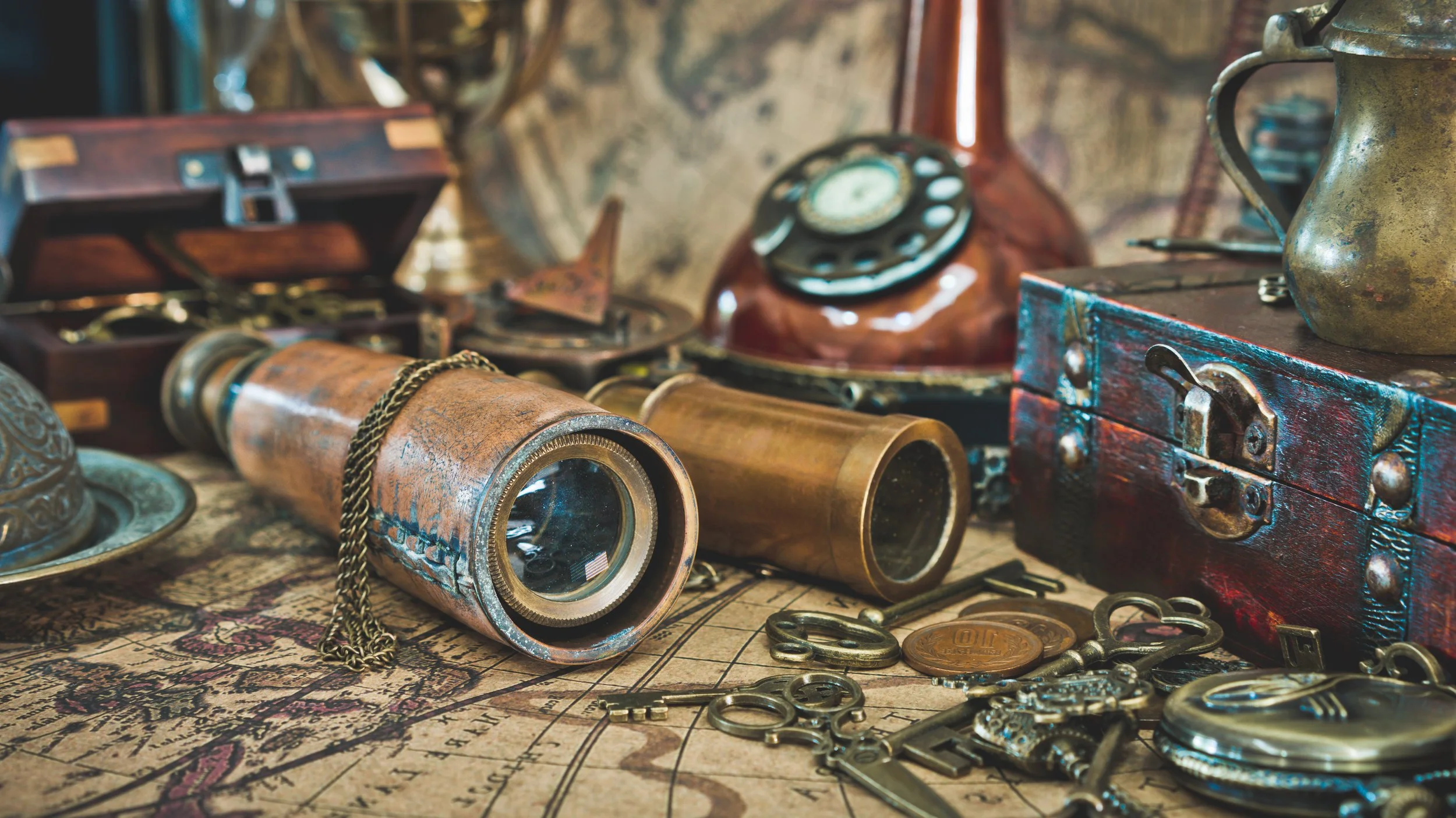 Vintage items including binoculars, an old telephone, a brass cup, a wooden box, scattered coins, keys, and an old map or document.