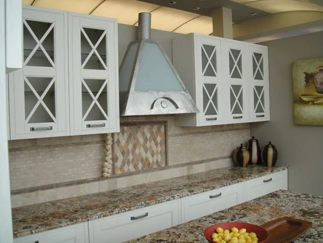 Kitchen with white cabinets, a granite countertop, a tile backsplash, and a stainless steel vent hood above the stove, and decorative vases on the counter.