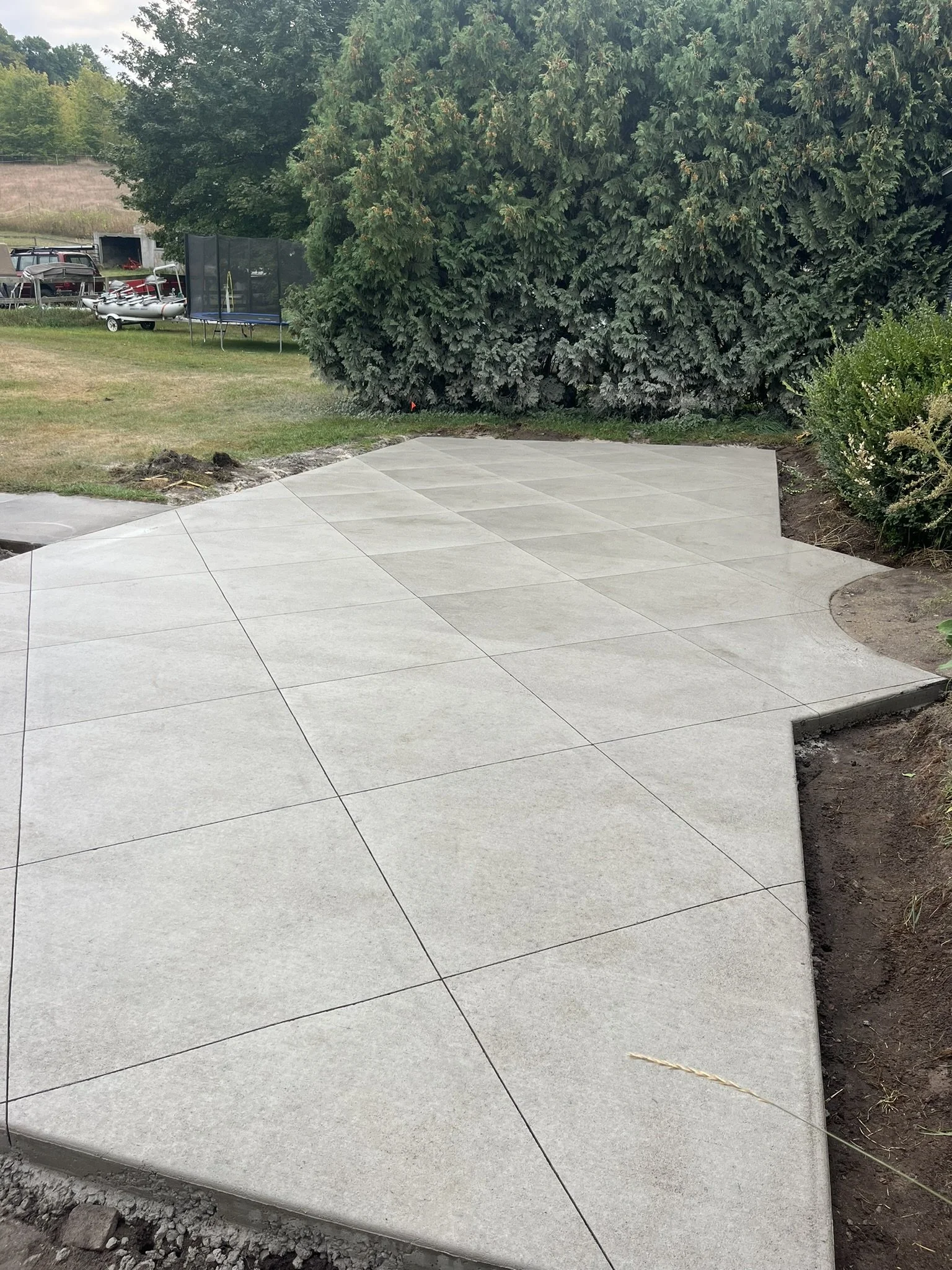 A newly poured concrete patio with visible expansion joints, surrounded by gardening and landscaping in a yard.