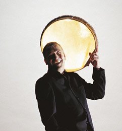 Abbi Patrix smiling and holding a large drum over his shoulder