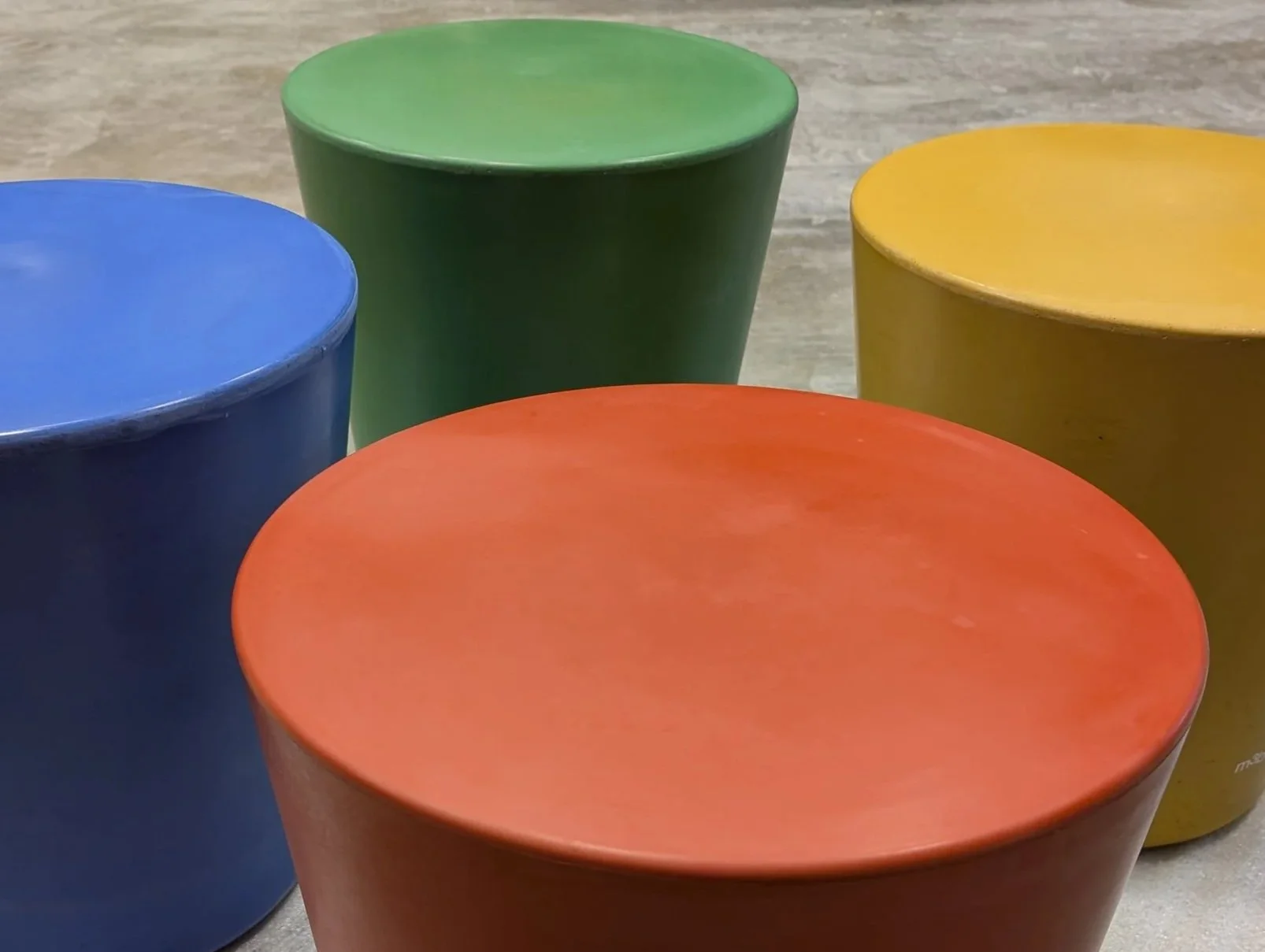 Cinq tabourets colorés en plastique, de couleur bleue, orange, verte, jaune et rouge, alignés sur un sol en bois.