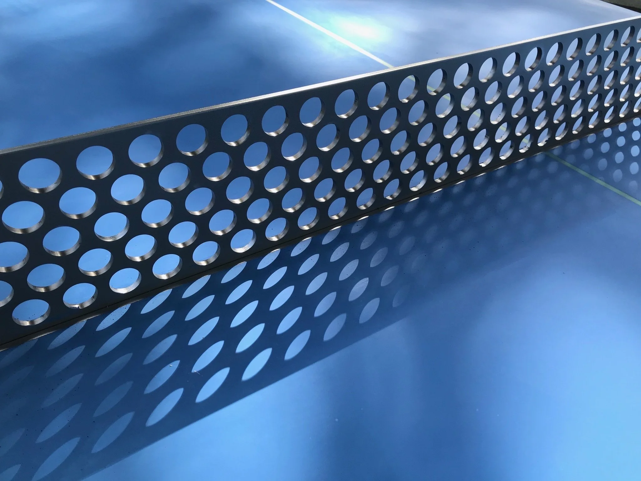 Une raquette de tennis en métal suspendue, créant une ombre circulare et une réflexion sur une surface bleue.