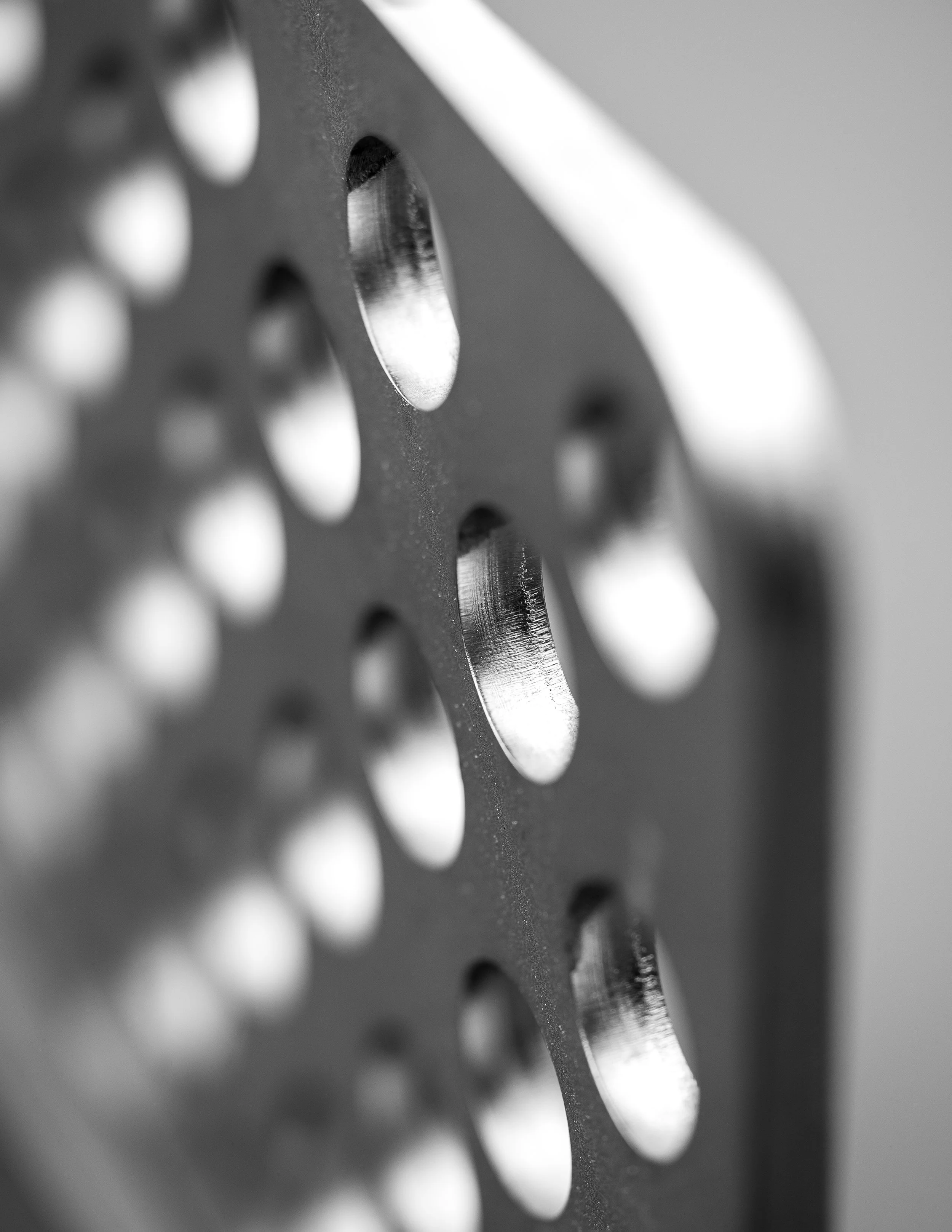 Close-up de la surface d'un outil de cuisine en acier inoxydable avec des trous ovales, vue en noir et blanc.