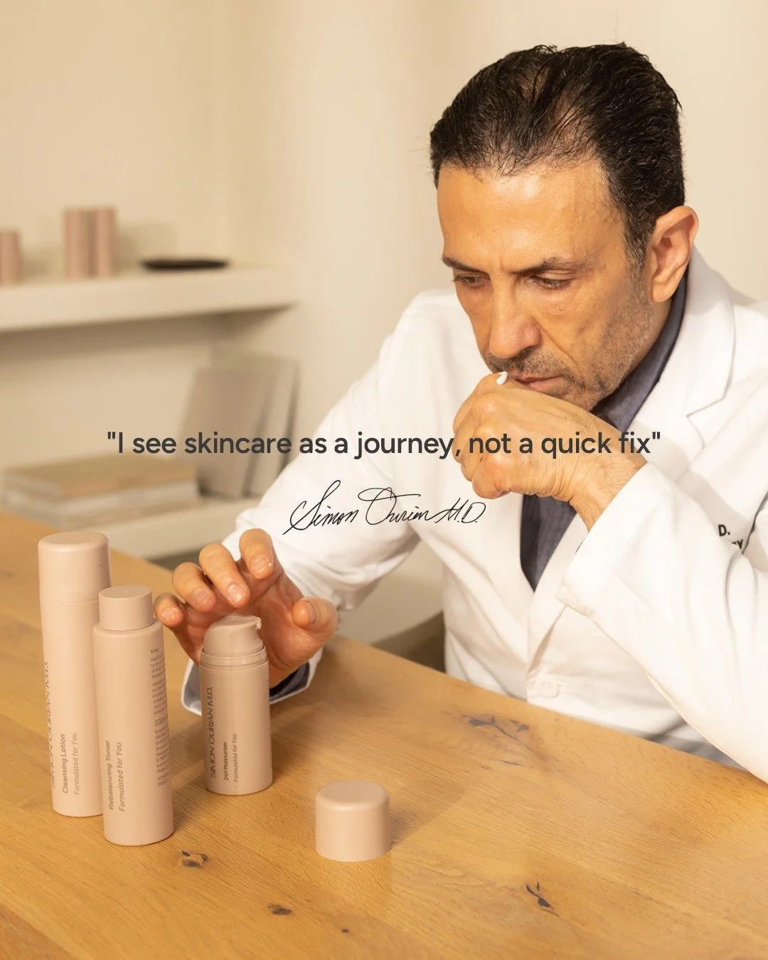 Un homme en blouse blanche regarde des produits de soin pour la peau posés sur une table en bois, avec une citation en français et la signature de Simon Ourain M.D.