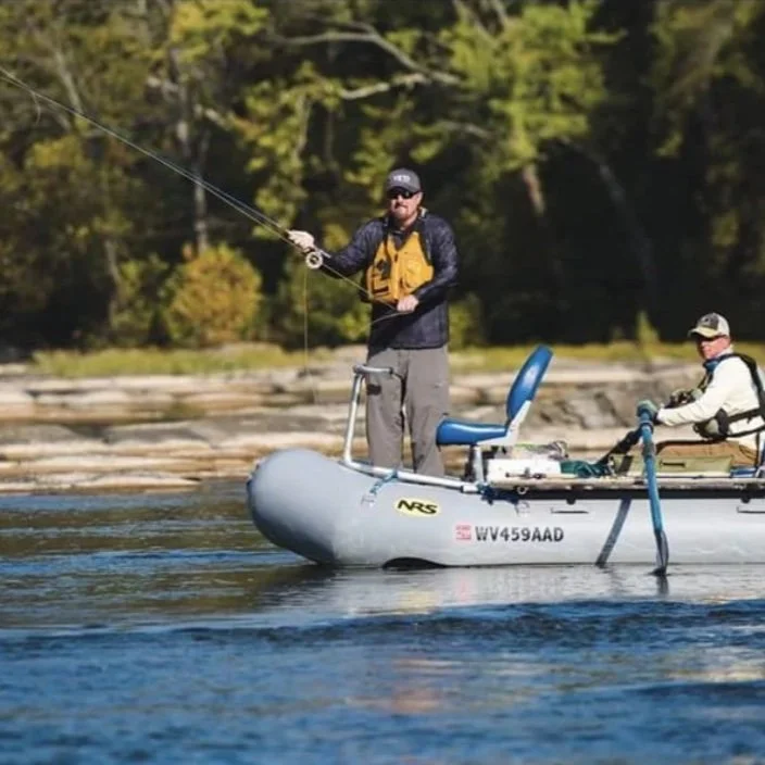 Two men fishing from an inflatable boat on a river, with trees in the background.