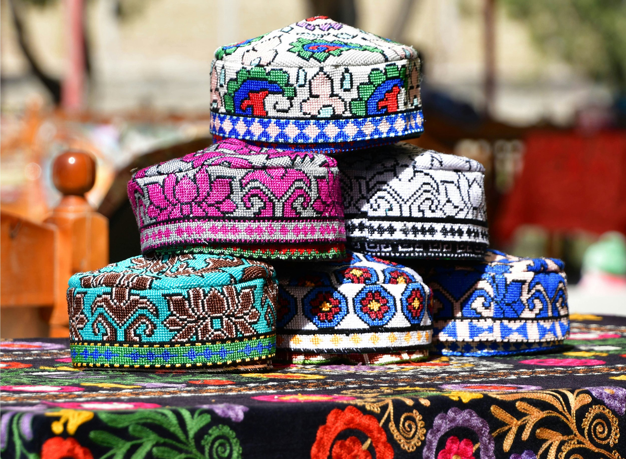 Stacked embroidered hats with traditional patterns on a floral embroidered surface, outdoors.