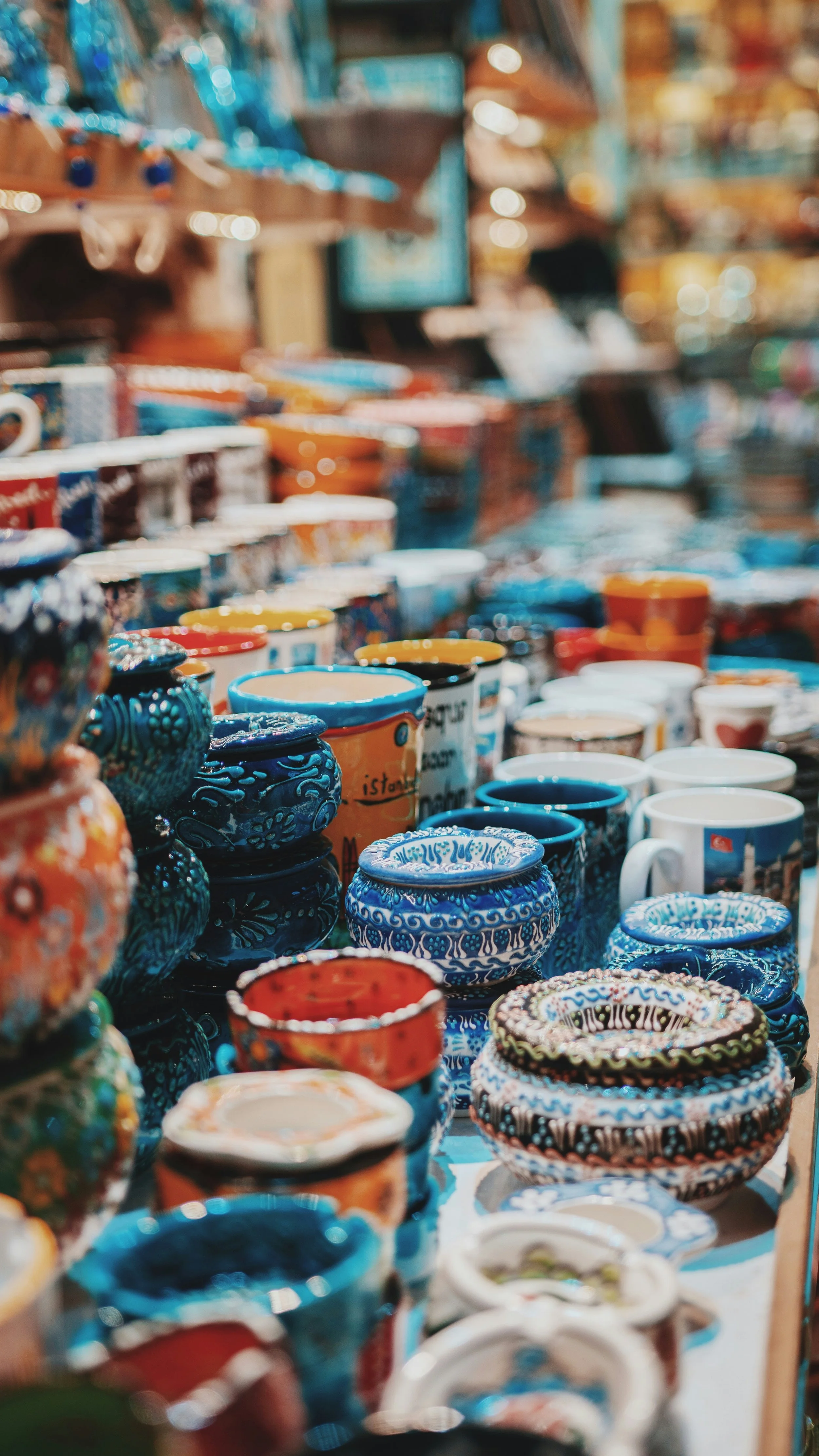 Colorful ceramic mugs and bowls arranged on a market stall, with shelves and a person in the background.