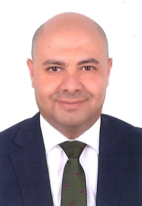 Headshot of a bald man wearing a dark suit, white shirt, and green tie, smiling at the camera.
