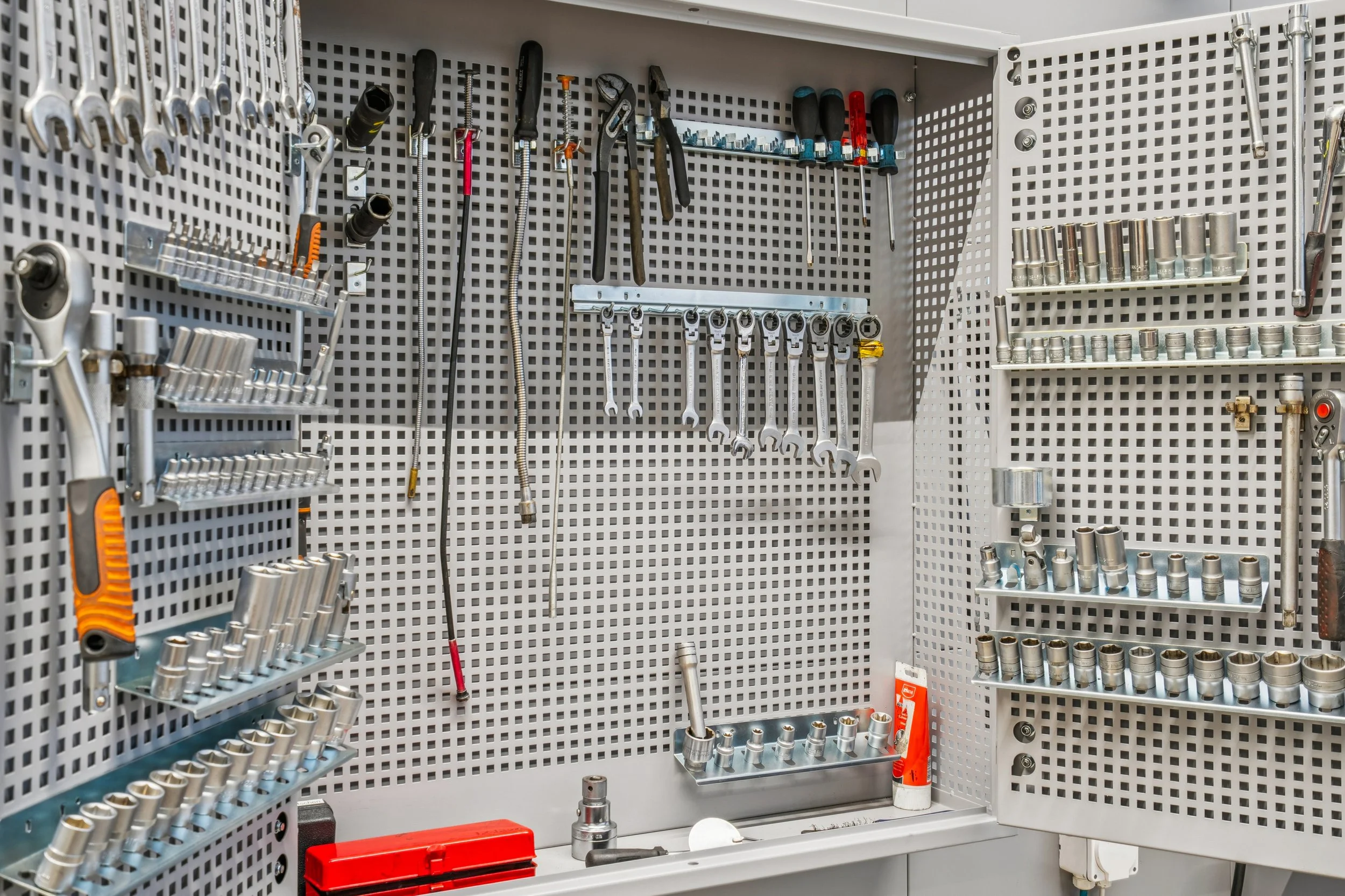 Werkzeugwand mit Schraubenschlüsseln, Schraubendrehern, Stecknüssen und anderen Werkzeugen ordentlich aufgehängt.