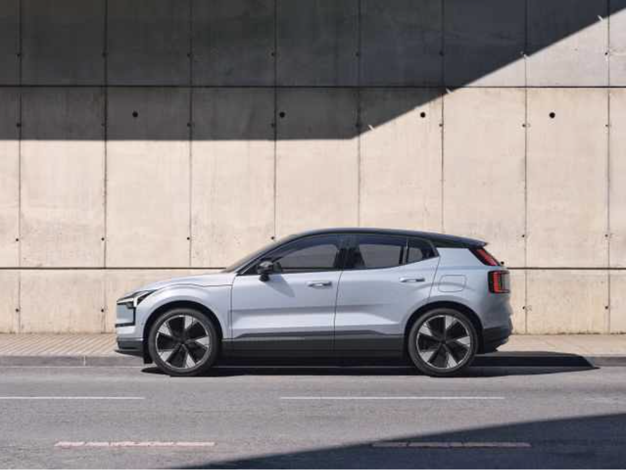 Ein silbernes SUV parkt an einer Stadtstraße vor einer Betonmauer, Schatten fällt auf die Mauer.