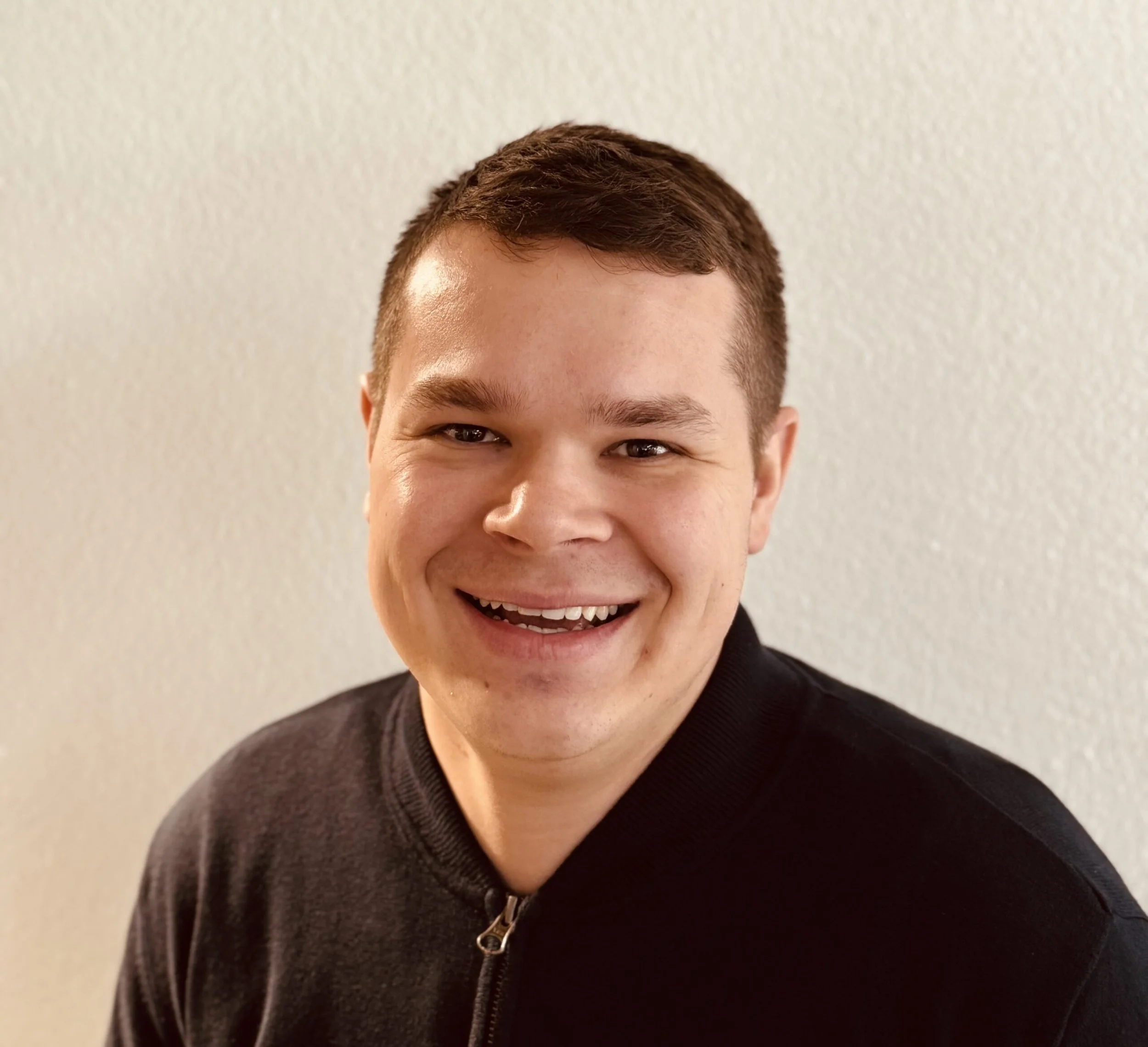 Junge Mann lächelt vor einer hellen Wand.