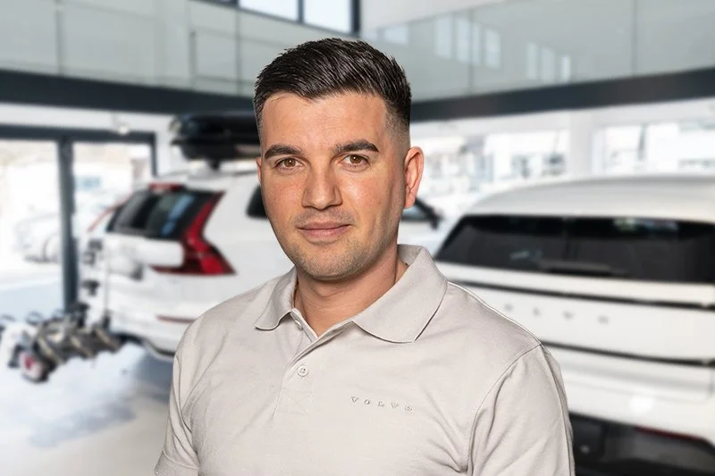 Porträt eines Mannes mit dunklen Haaren vor weißer Wand, trägt eine schwarze Jacke.