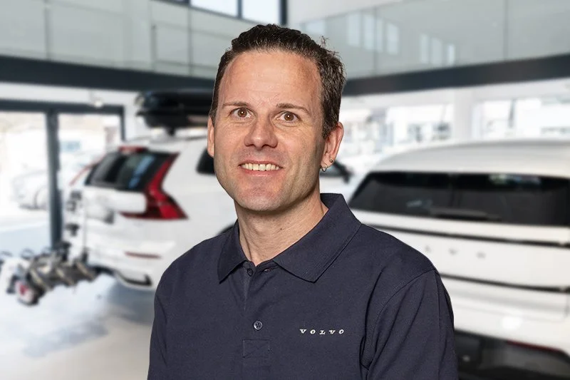 Porträt eines Mannes mit dunklem Haar, Eilend, in schwarzem Zipper, vor hellem Hintergrund.