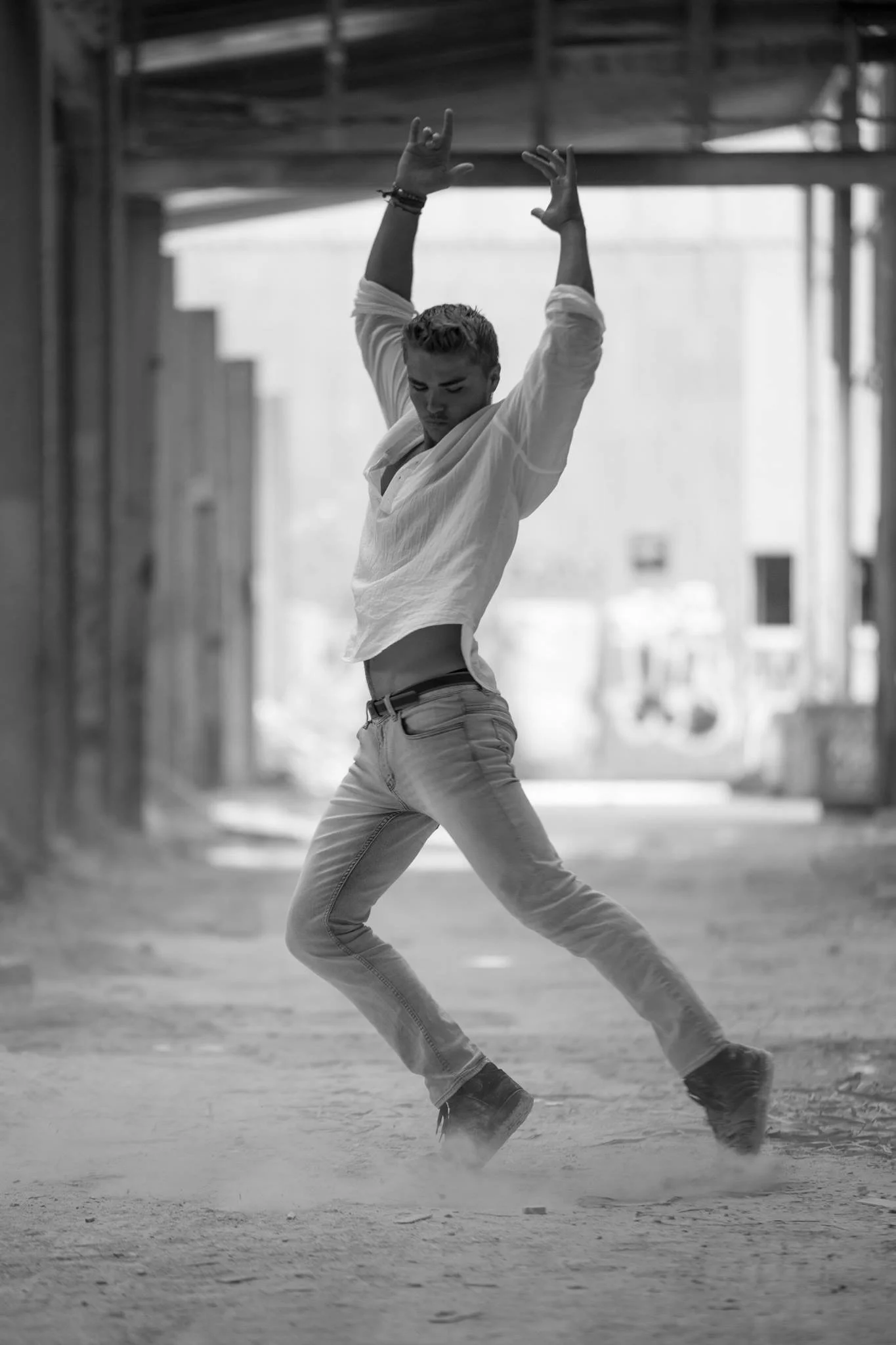 Jackson Kubian dancing outdoors in an urban area, wearing jeans and a loose shirt, with arms raised and a focused expression.