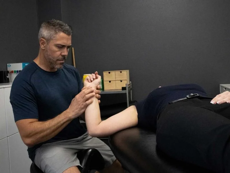 Suncoast Myotherapy - performs an arm strength test on a woman lying on an examination table in a medical setting.