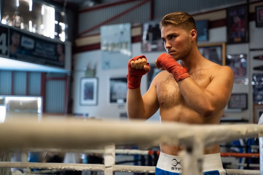 Jackson Kubian acting in a short film inside a gym, shirtless, with red hand wraps, standing in a fighting stance, and looking focused.