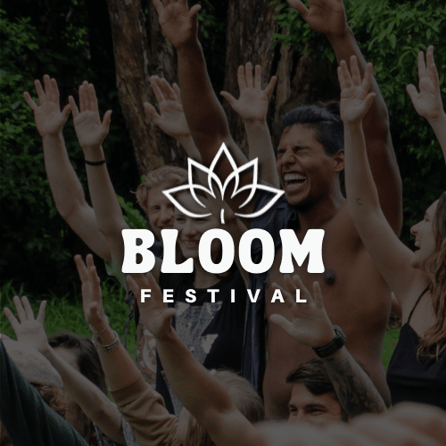 Group of diverse smiling people raising their hands outdoors at Bloom Festival in a green, wooded area.