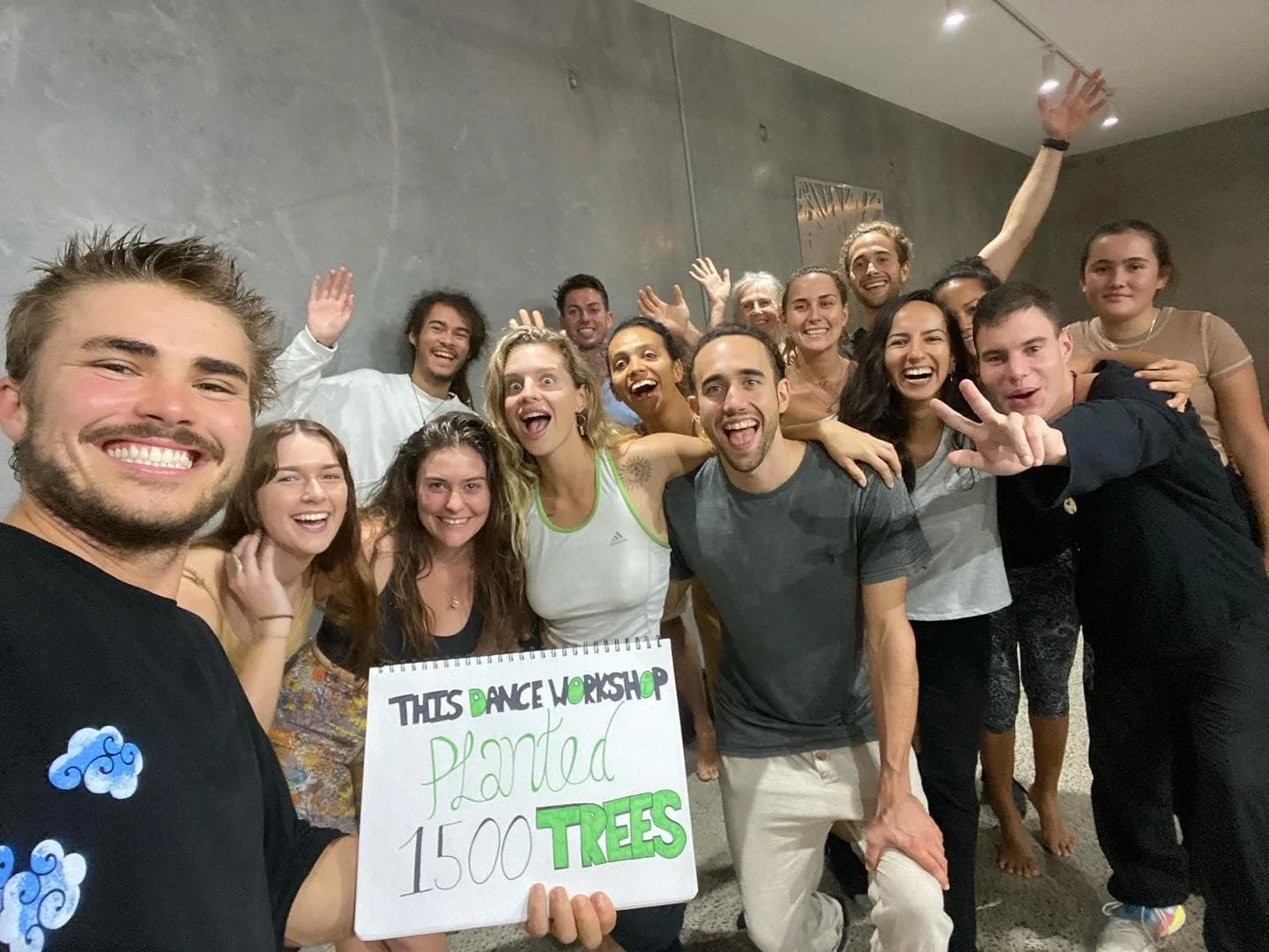 Transformational Dance Workshop - Jackson Kubian - A group of smiling people posing together indoors, holding a sign that says 'This dance workshop planted 1500 TREES'.