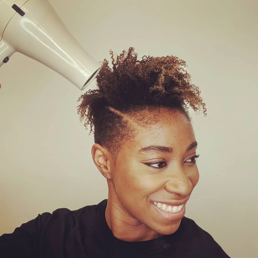 Woman smiling with a curly hairstyle being dried with a hairdryer.