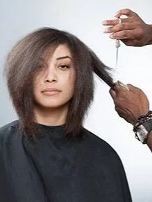 A woman getting her hair cut at a salon, with a stylist using scissors to trim her hair.