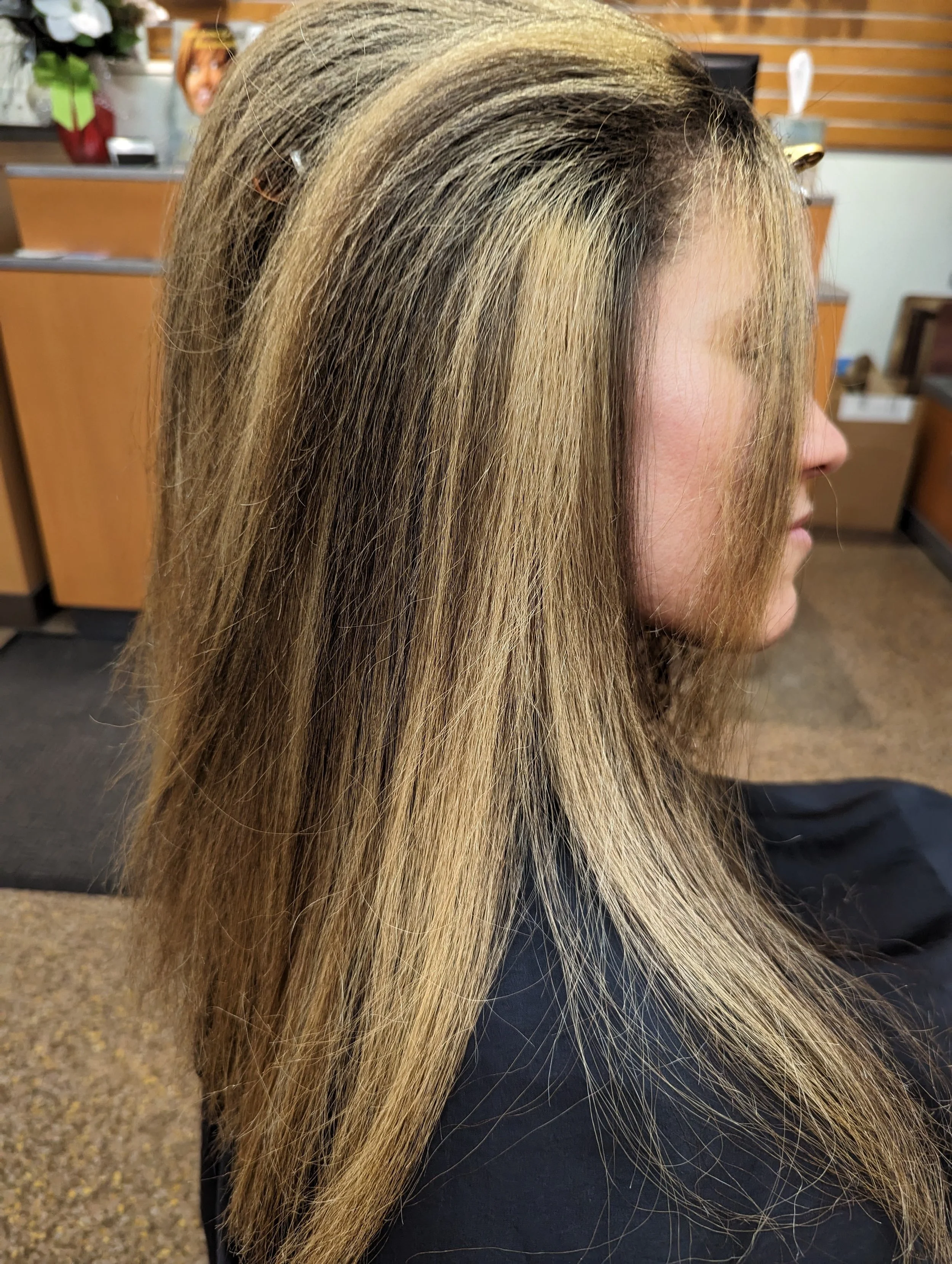 Side view of a woman with long, straight, blonde hair in a salon.
