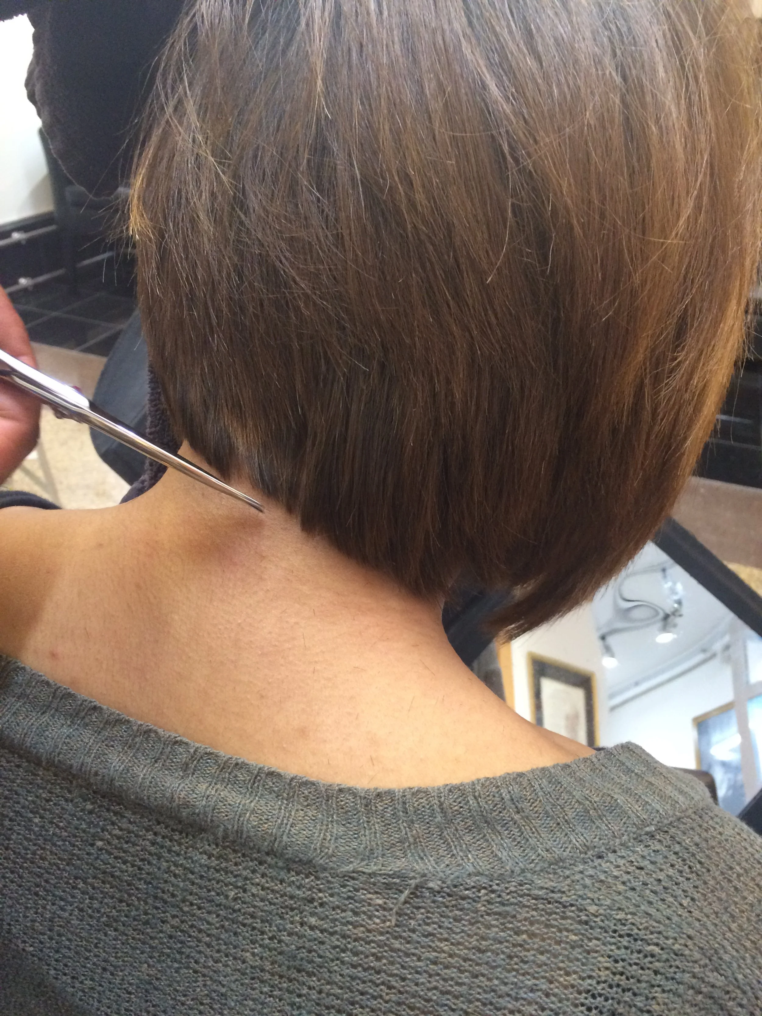 A person with short brown hair getting a haircut with scissors at a salon.