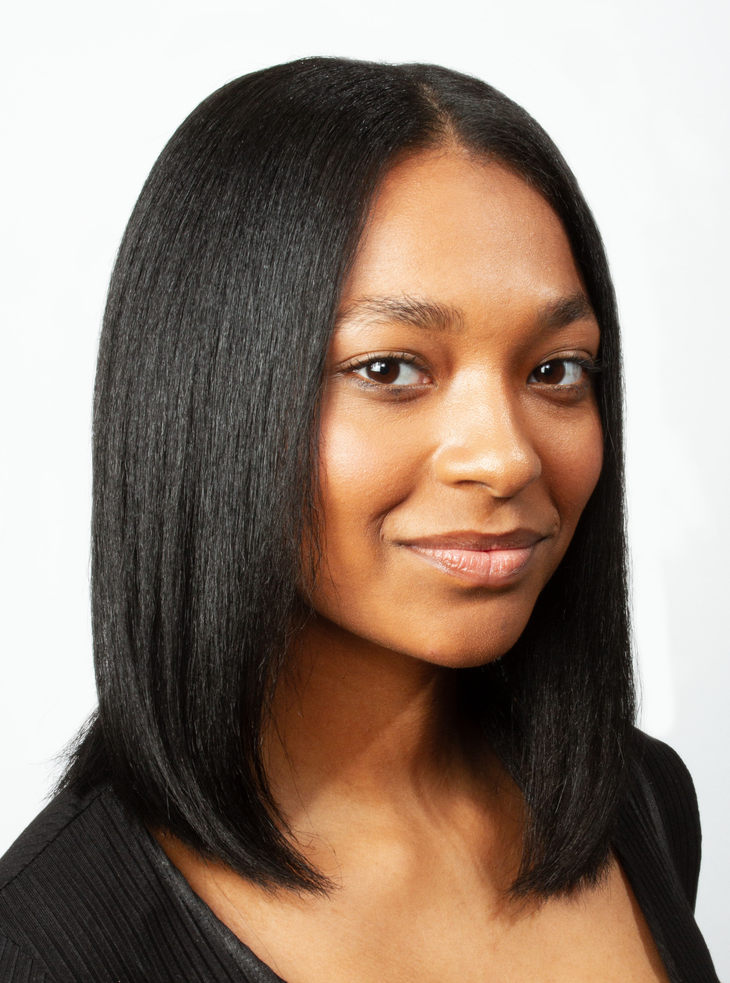 Close-up portrait of a young African American woman with straight black hair, wearing a black top, smiling softly against a plain white background.