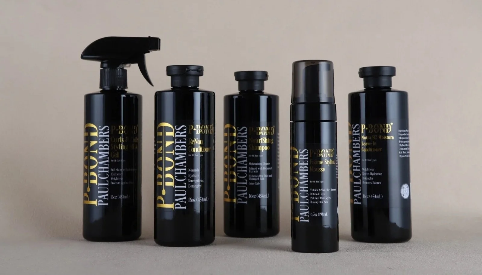 Five black bottles of Paul Mitchell hair care products arranged on a beige surface against a plain beige background.