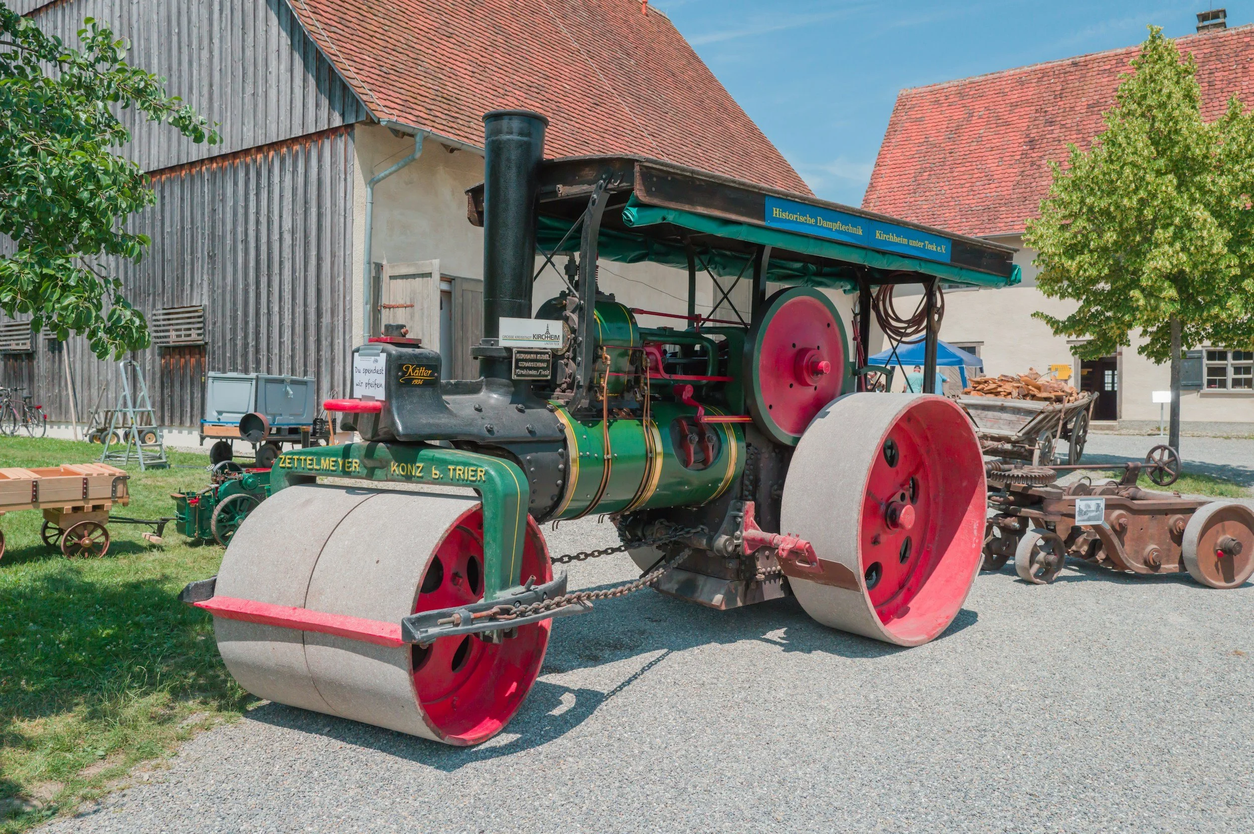 Vintage steamroller on display outdoors with a building and trees in the background.