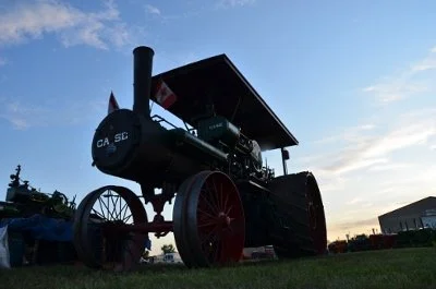 A vintage steam-powered tractor on a grassy field during sunset