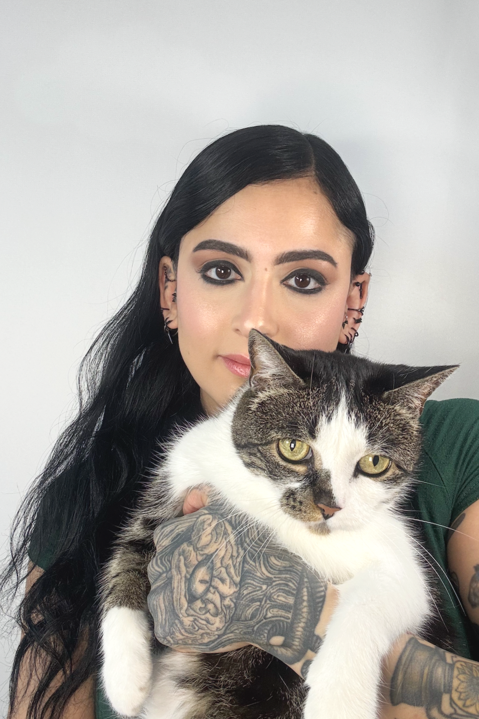 A woman with black hair and tattoos holding a domestic short-haired cat with white and tabby fur.