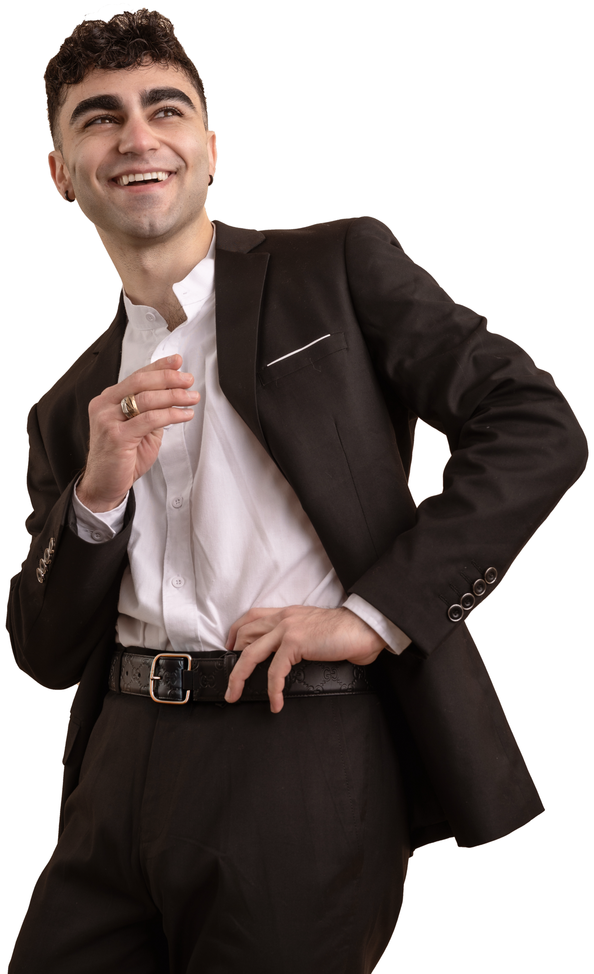 A young man smiling, dressed in a black suit and white shirt, with one hand on his hip and the other near his collar, posing confidently against a black background.