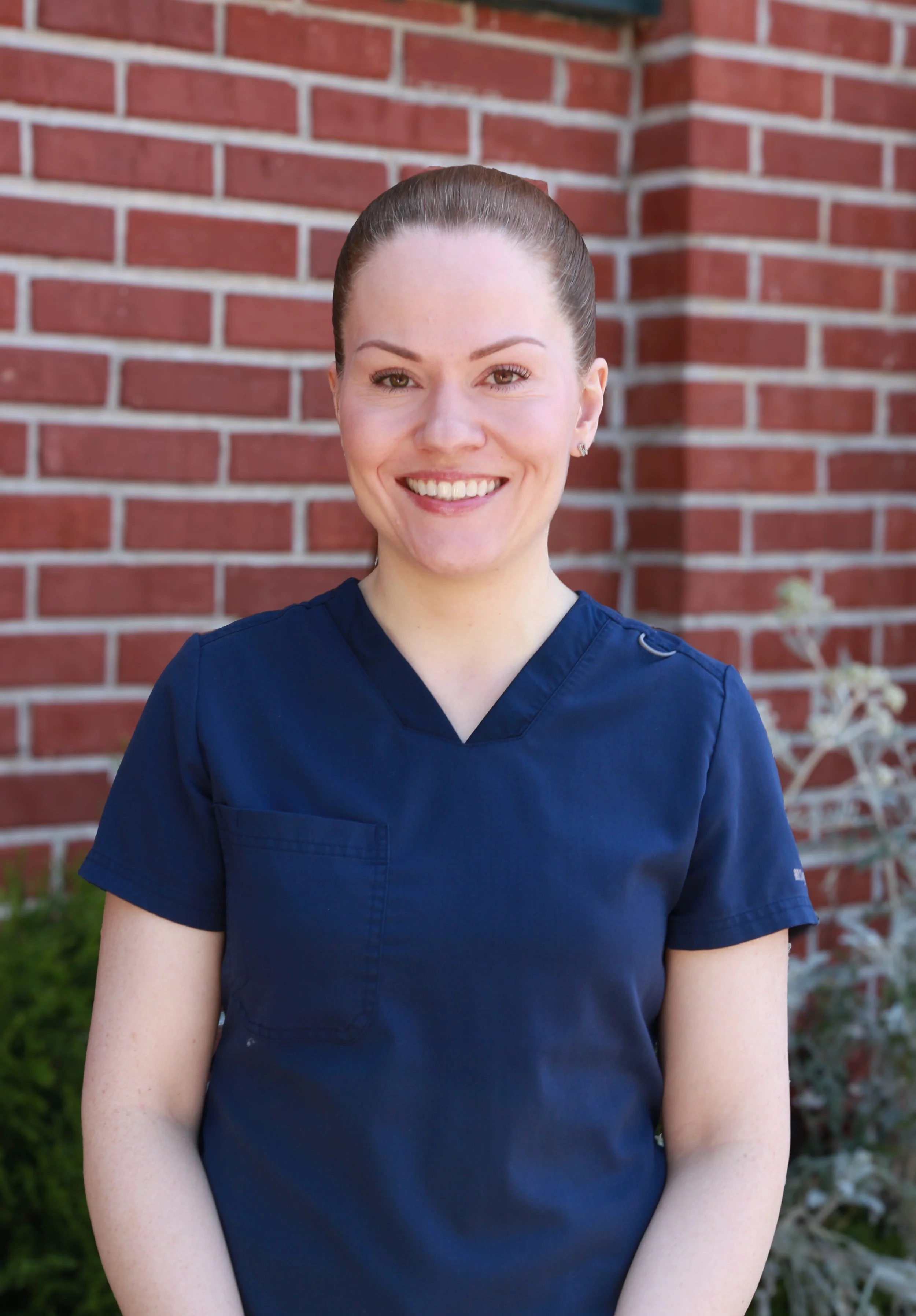 Smiling woman in navy scrubs standing in front of a brick wall