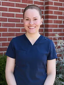 Smiling woman in navy scrubs standing in front of a brick wall
