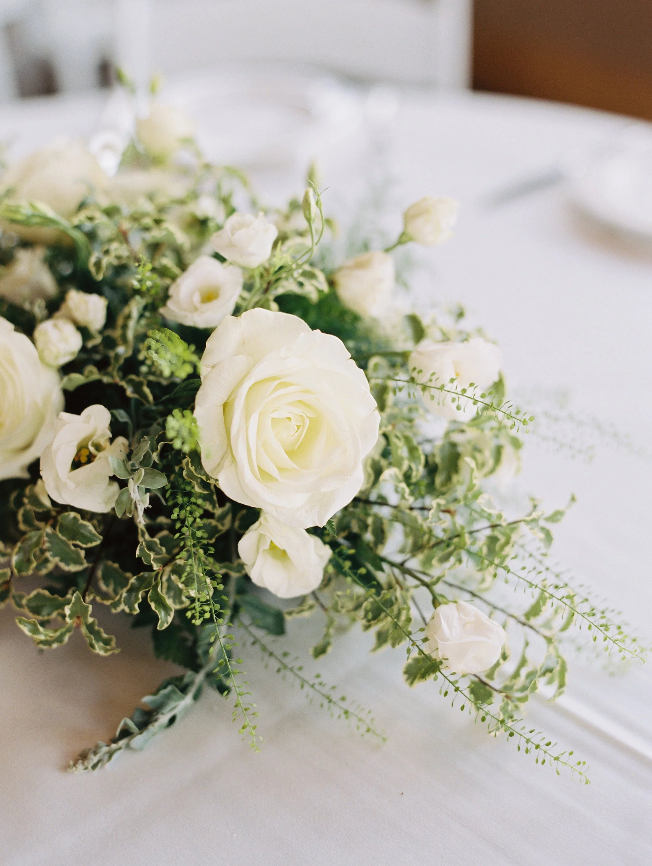Close-up of a white floral centerpiece with roses and greenery on a white tablecloth.
