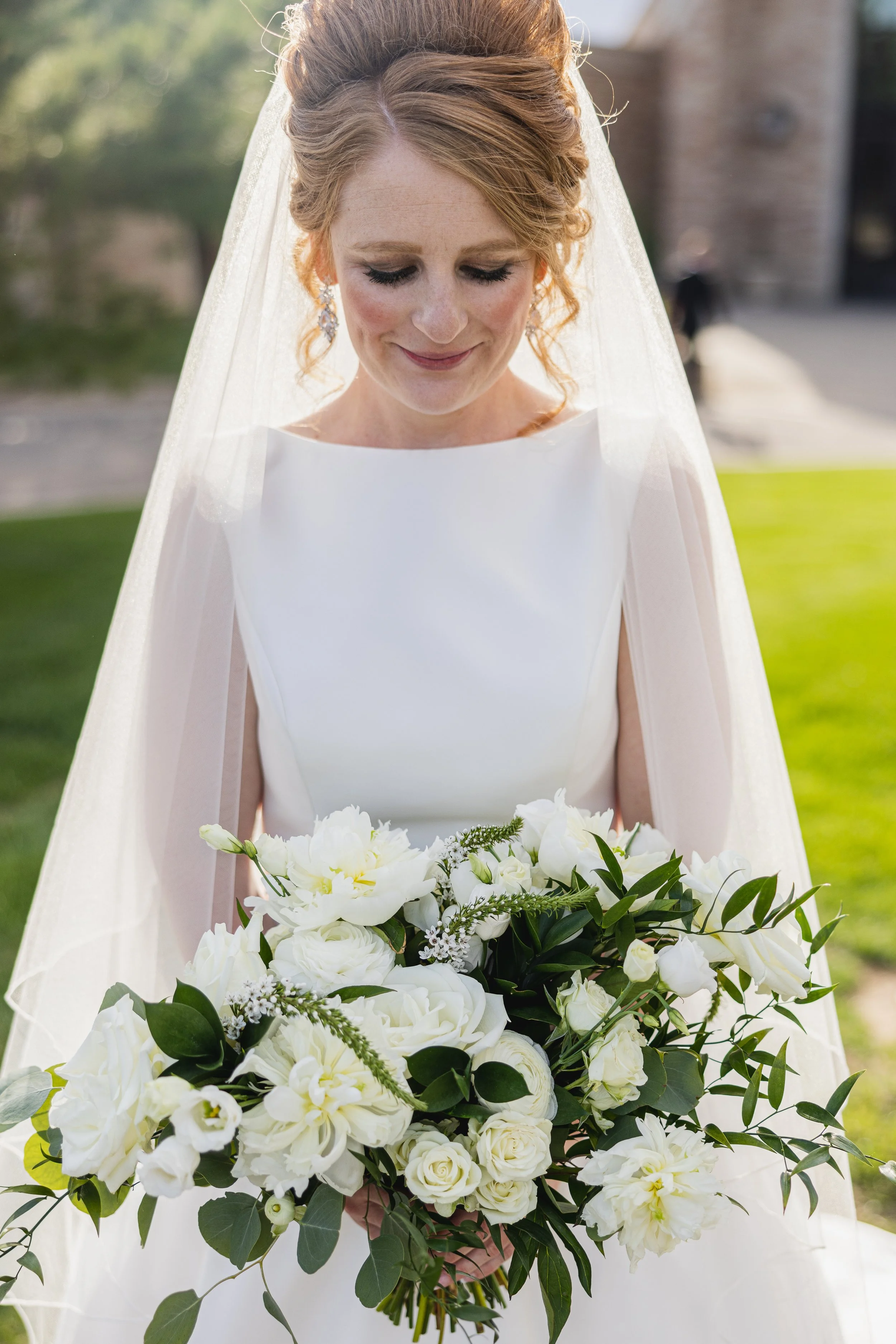 A bride with red hair in a white wedding dress holding a bouquet of white flowers