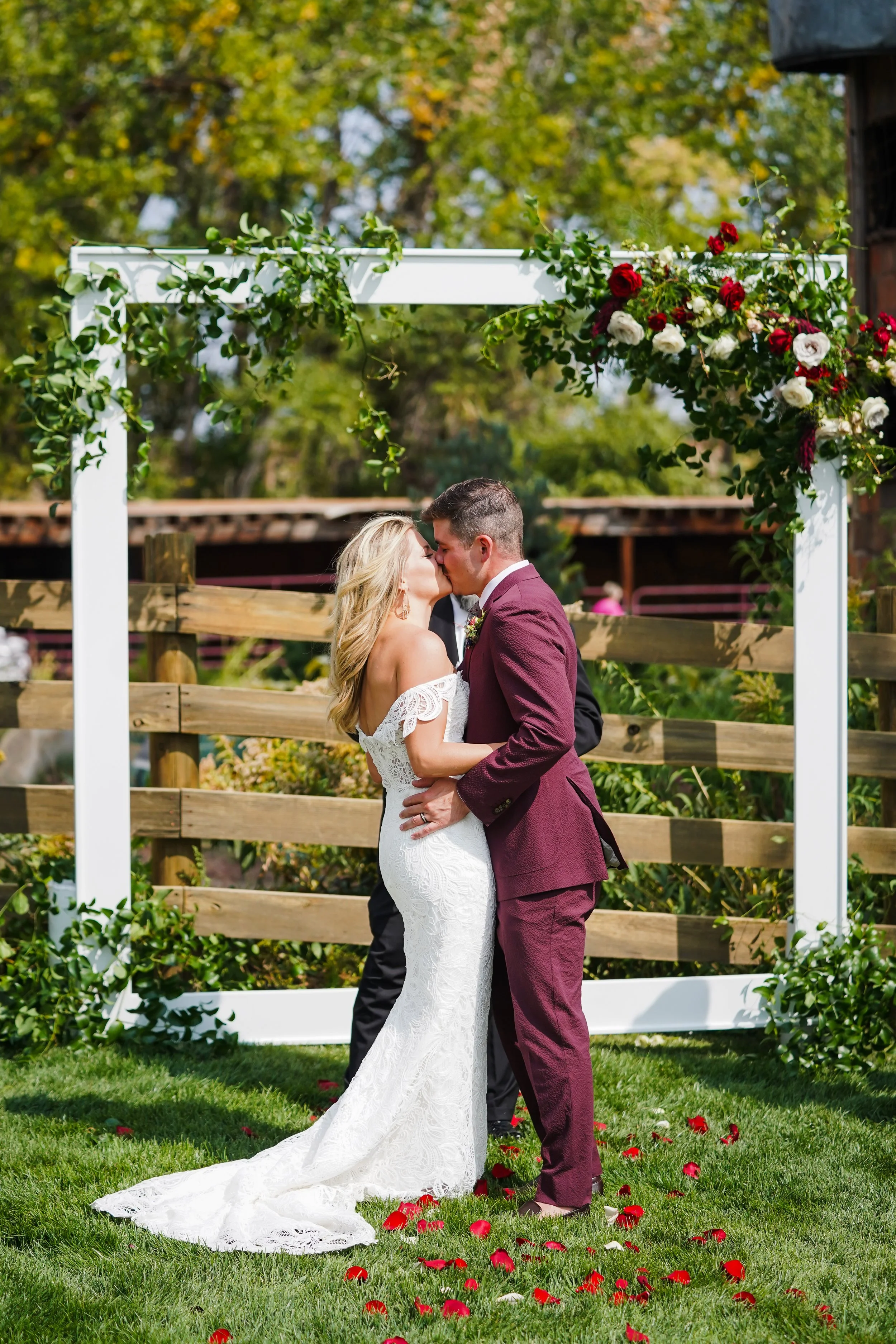 A newlywed couple sharing a kiss under a decorated wedding arch outdoors.