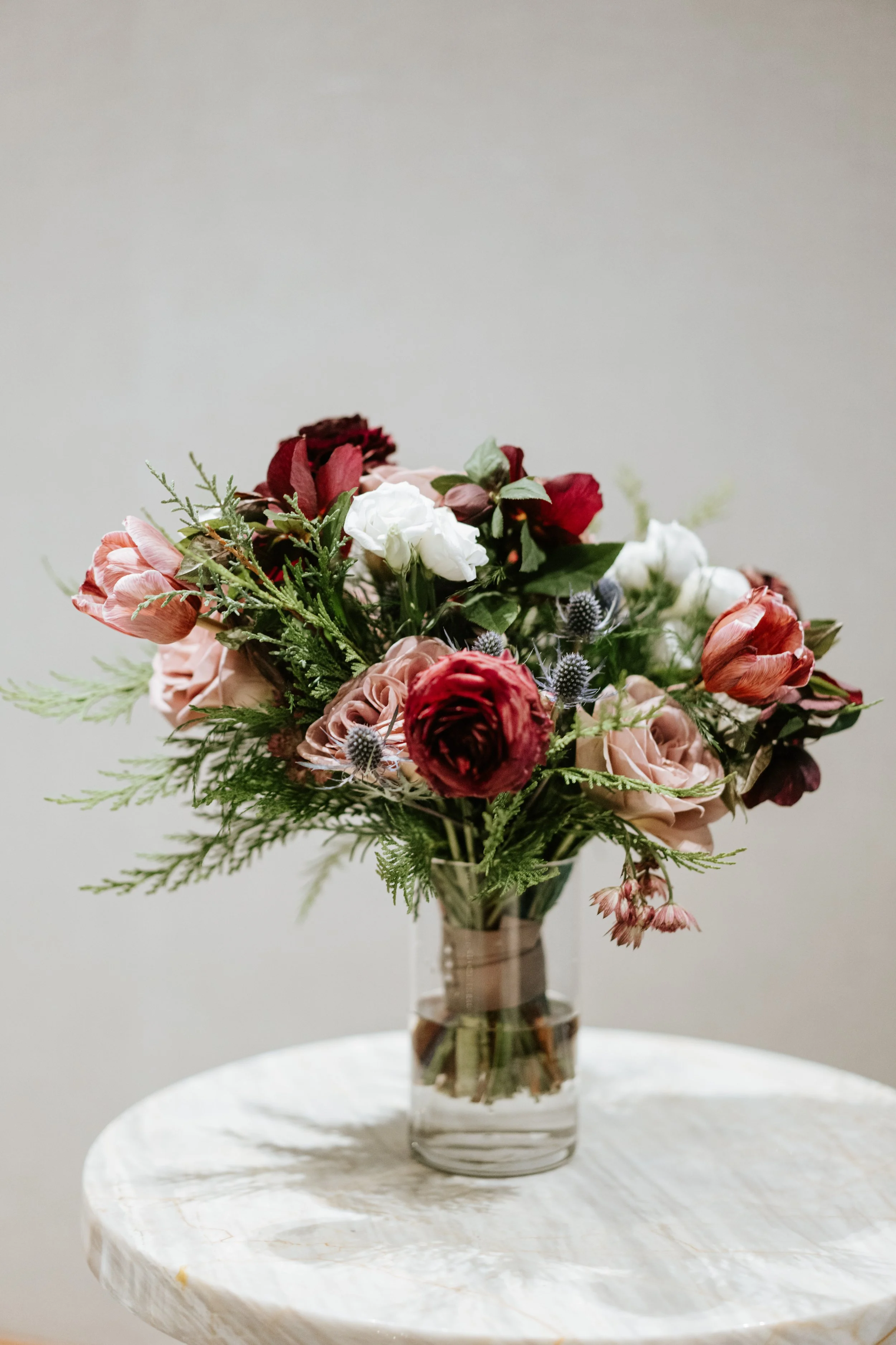A bouquet of mixed flowers in pink, white, red, and purple, arranged in a clear glass vase on a white marble table.