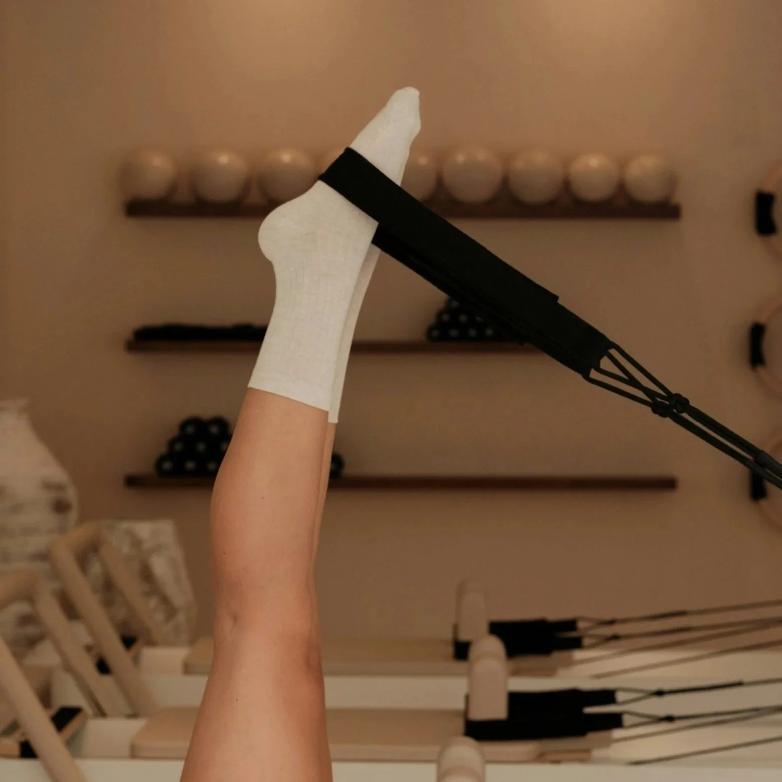 A person's leg raised in the air with a white bandage around the ankle, holding a Pilates resistance band.