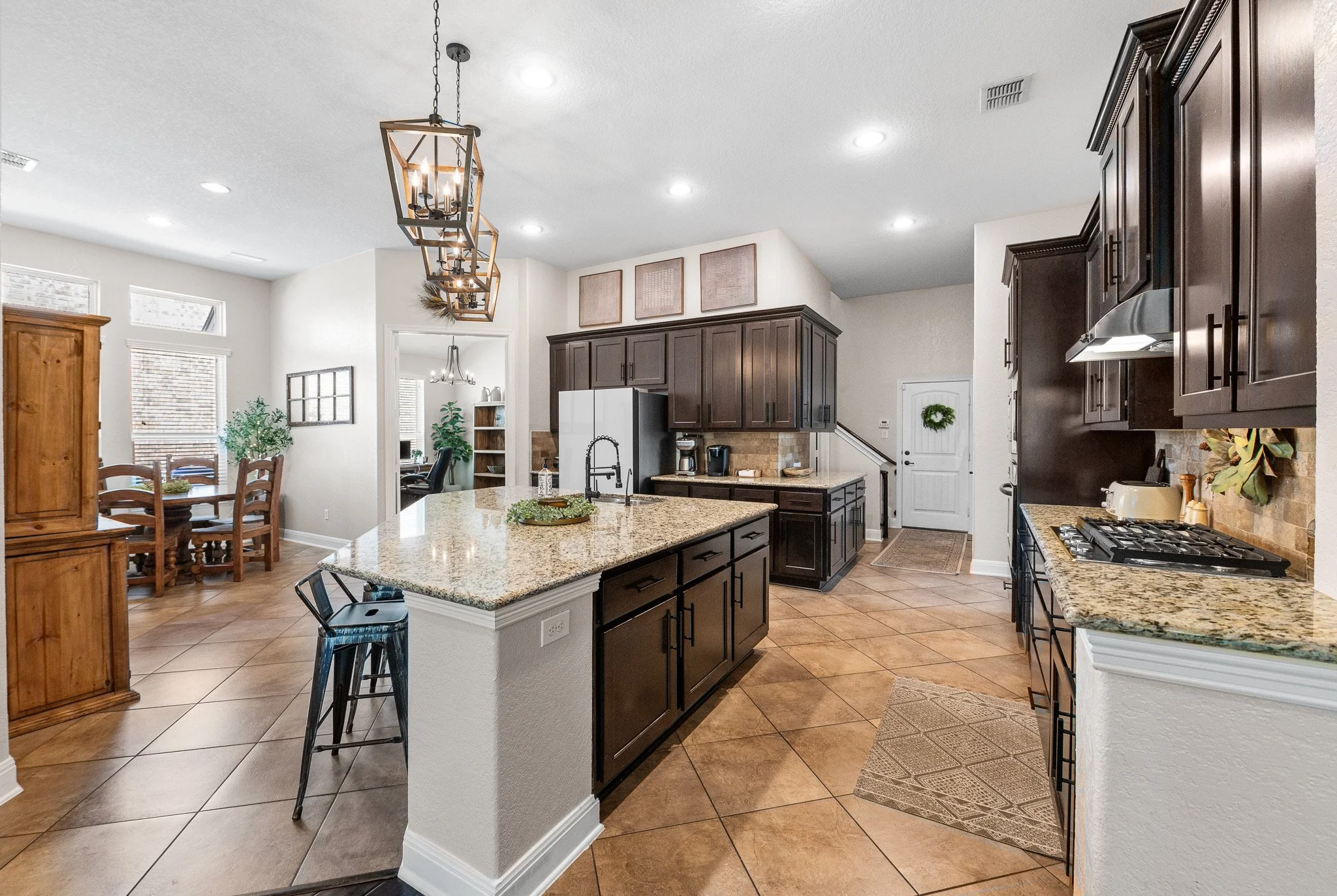 Modern open-concept kitchen with dark wood cabinets, granite countertops, a kitchen island, and tiled floors, connecting to a dining area and living space.