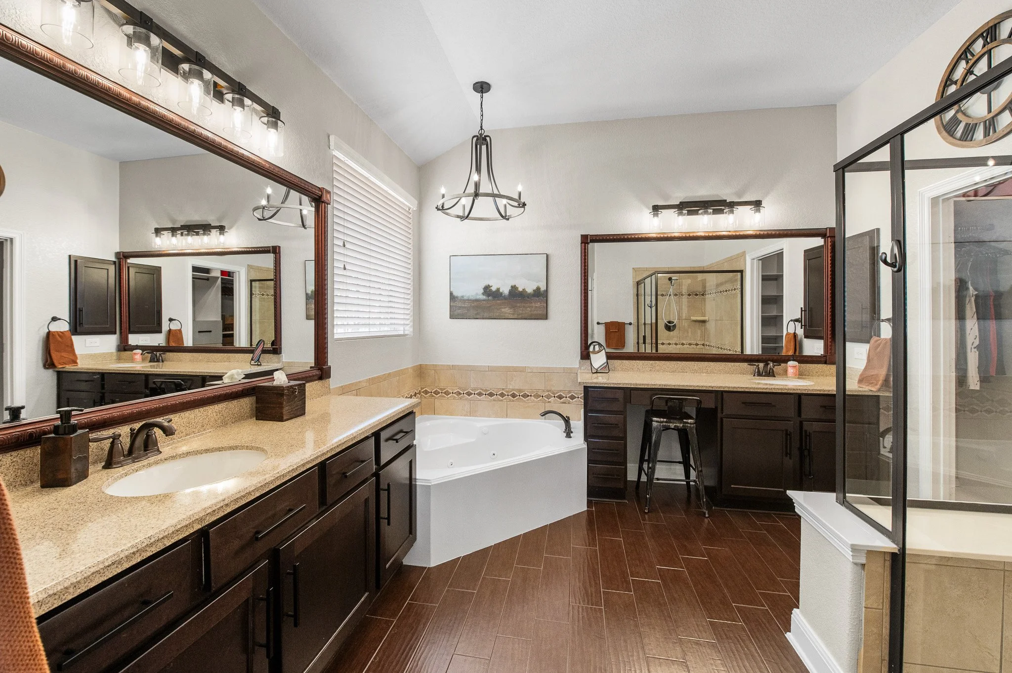 A spacious modern bathroom with a double vanity with dark wood cabinets and beige countertops, a large mirror, a bathtub, a walk-in shower with glass doors, and a window with blinds.