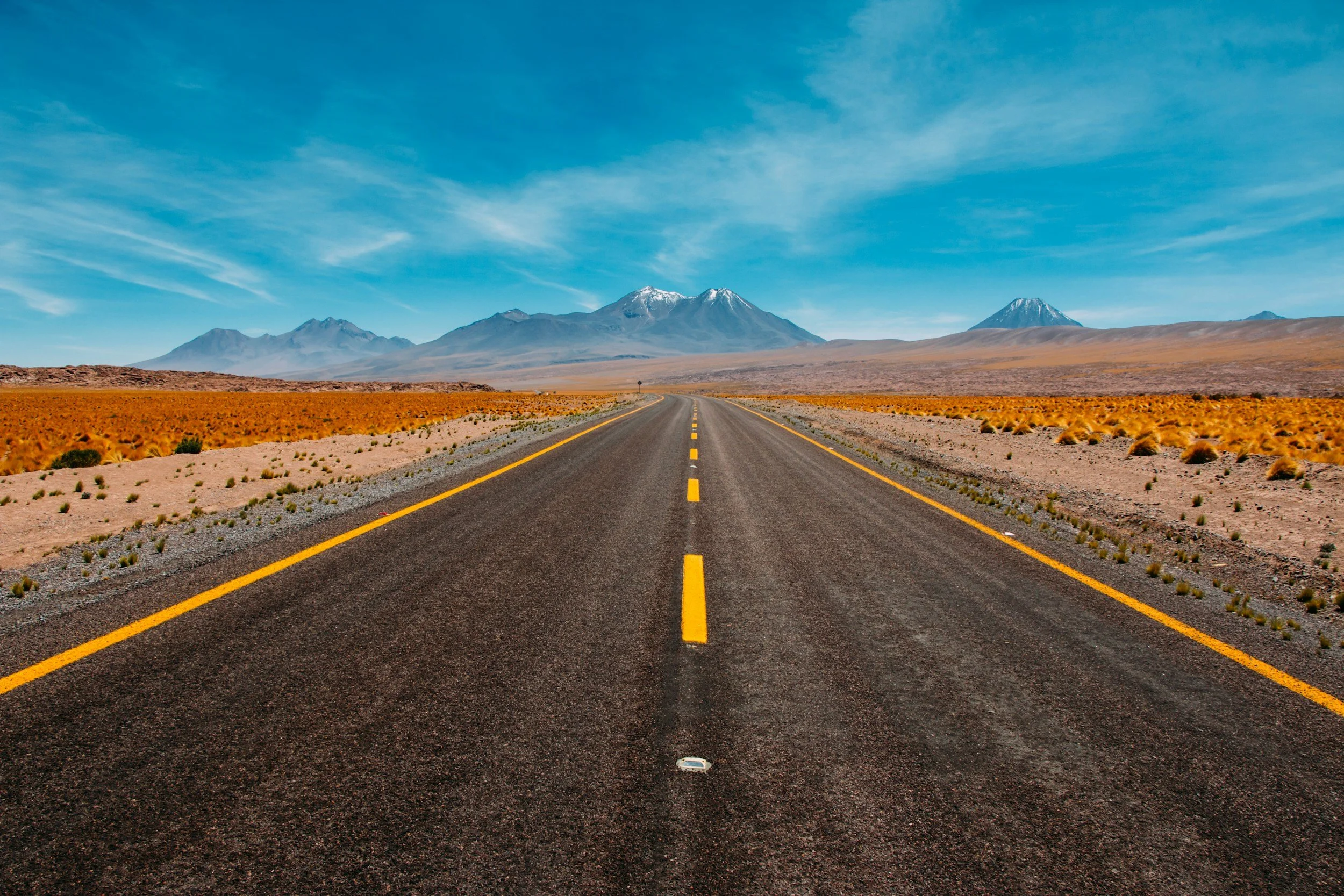 long empty road extending through a desert landscape with mountains in the distance and a clear blue sky overhead