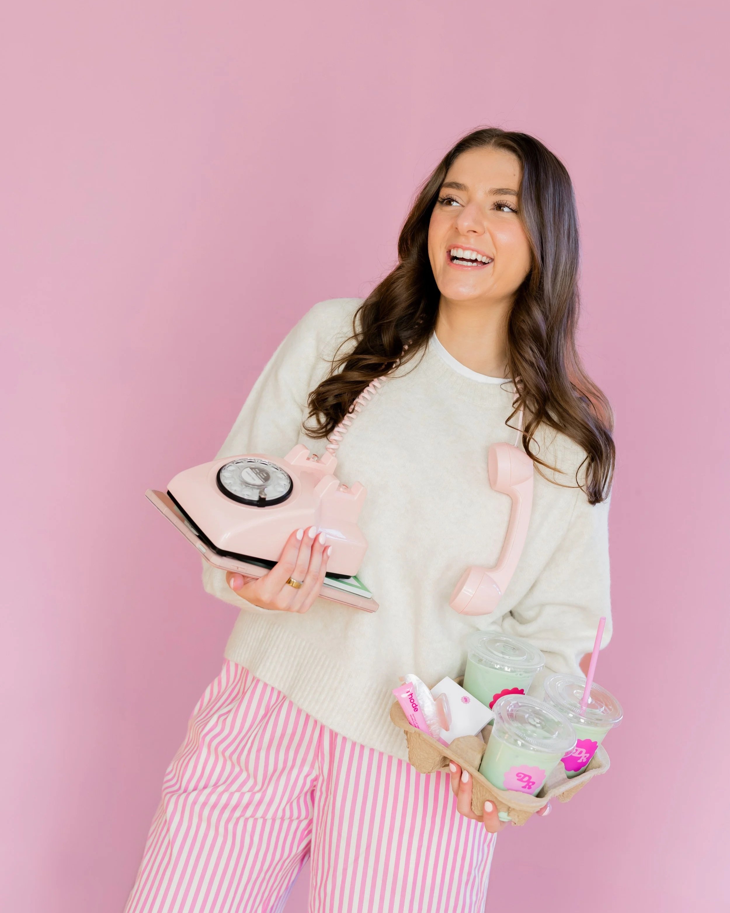 Instagram coach managing client communications with pink phone while holding branded matcha drinks