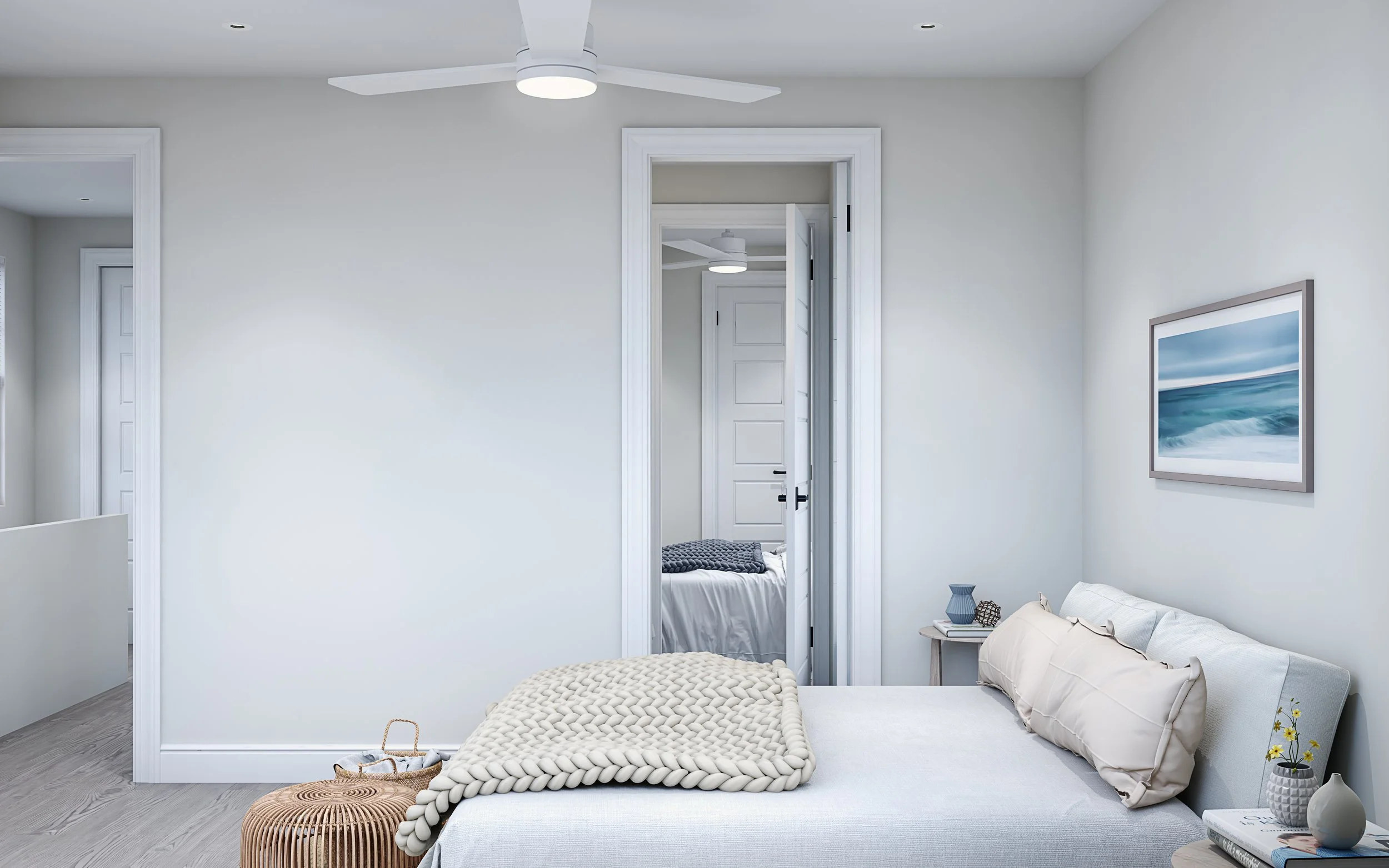 A bright, modern bedroom with light-colored walls and a ceiling fan. There is a bed with pillows and a chunky blanket, a nightstand with decorative items, and a framed seascape painting on the wall. An open door leads to another room with a bed visib