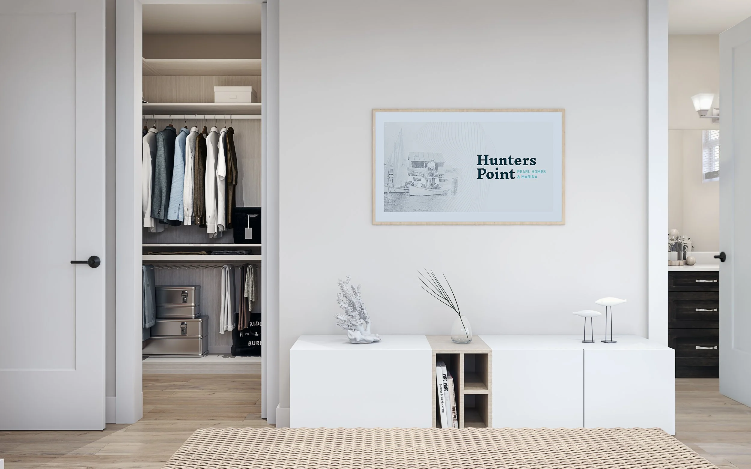 Interior view of a bedroom with an open closet on the left, a white wall with a framed picture in the center, and a white cabinet with decorative objects on top. The closet contains hanging clothes and storage boxes.