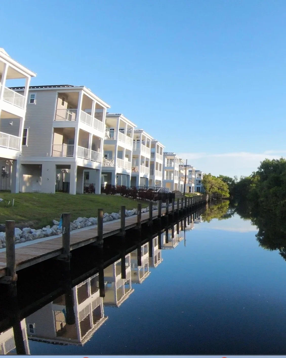 Residential buildings with balconies beside a waterway reflecting the structures under a clear blue sky.