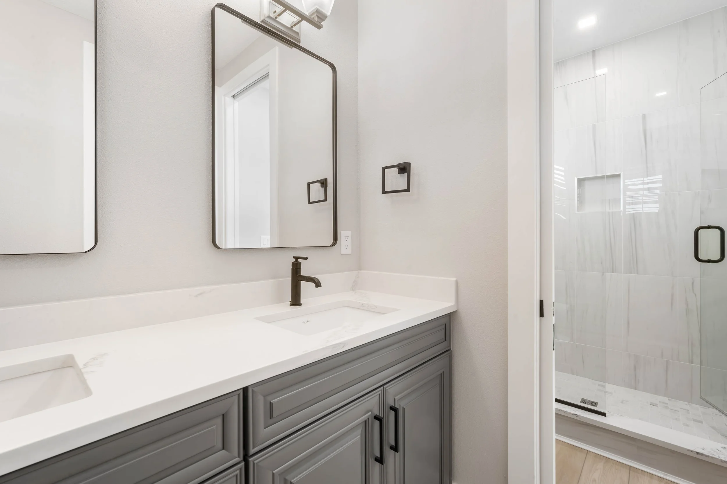 Modern bathroom with white vanity, two mirrors, and a glass-enclosed shower with marble tiles.