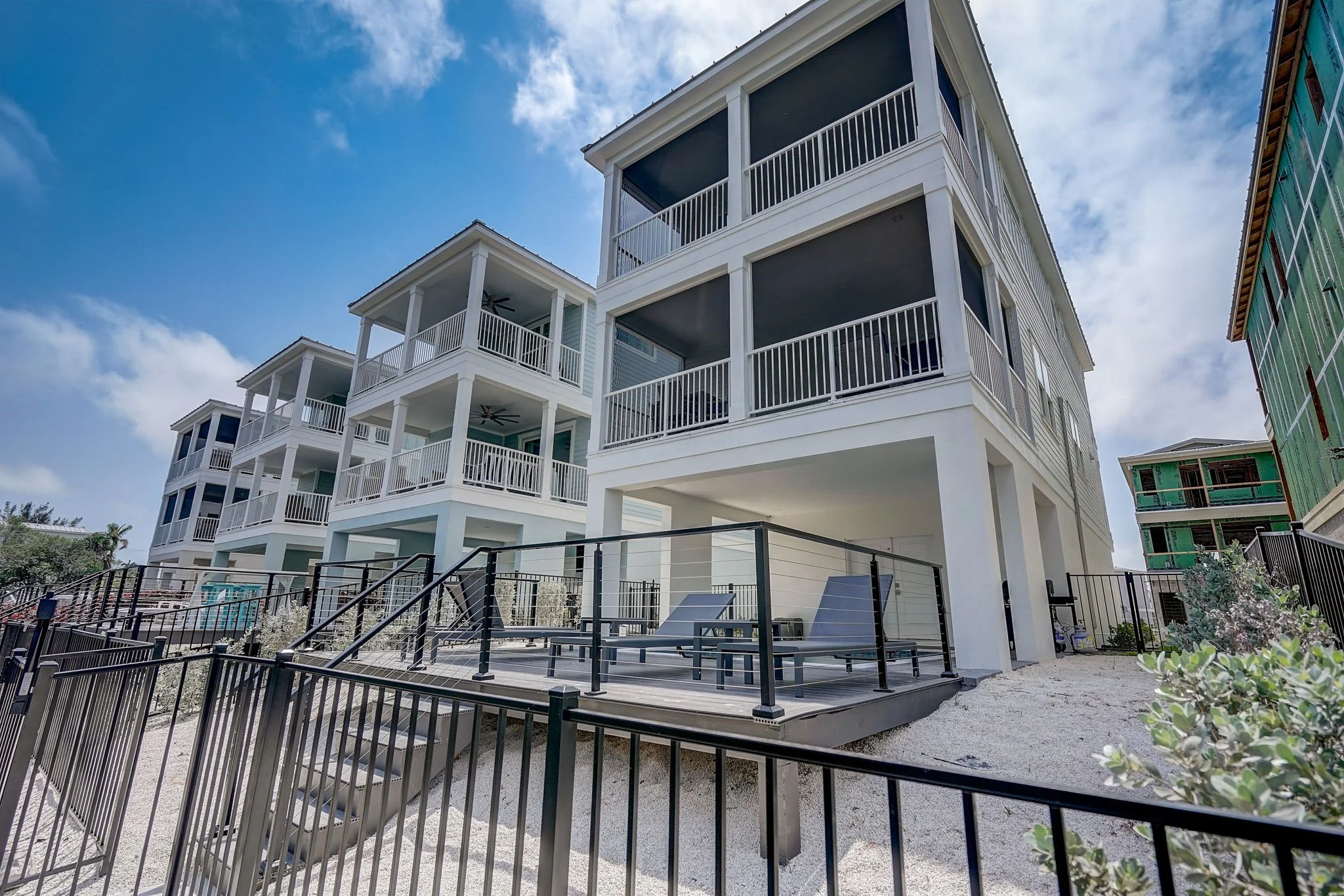 Multiple modern white and green multi-story buildings with outdoor balconies and stairs, under a partly cloudy blue sky.