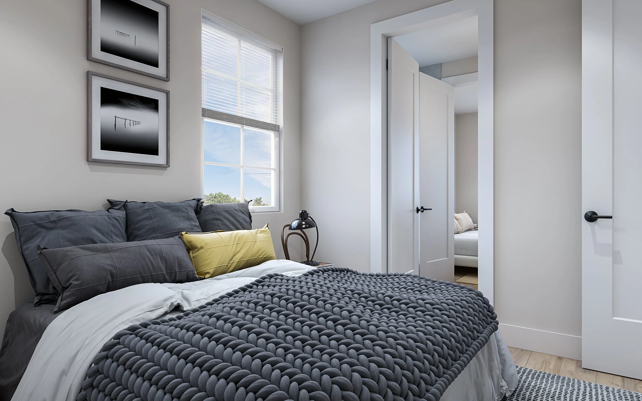 A modern bedroom with framed black-and-white landscape photographs above a bed with dark gray and yellow pillows, a textured gray blanket, a wooden nightstand, a black desk lamp, a window with blinds, and an open door leading to another room.