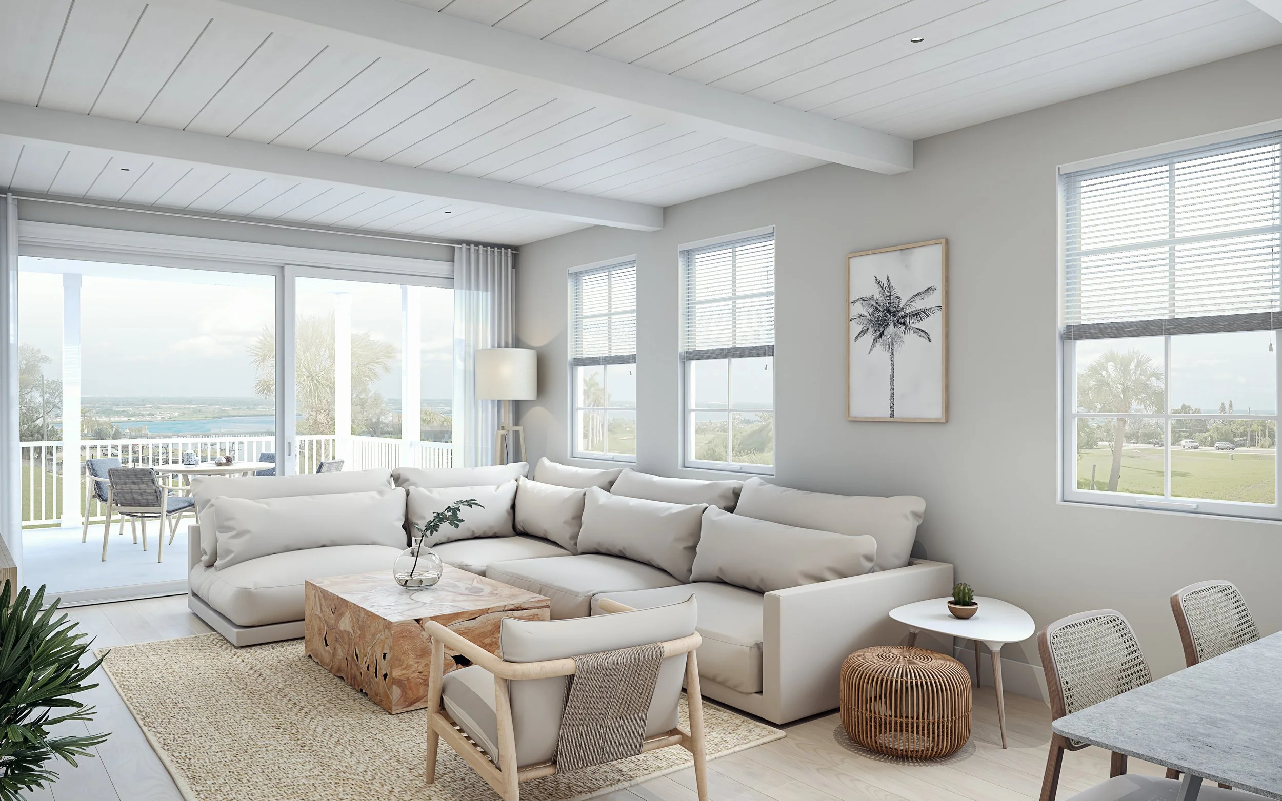 Bright living room with white sectional sofa, round white side table with potted plant, beige woven ottoman, picture of a palm tree on the wall, and large windows overlooking a lush green outdoor landscape.